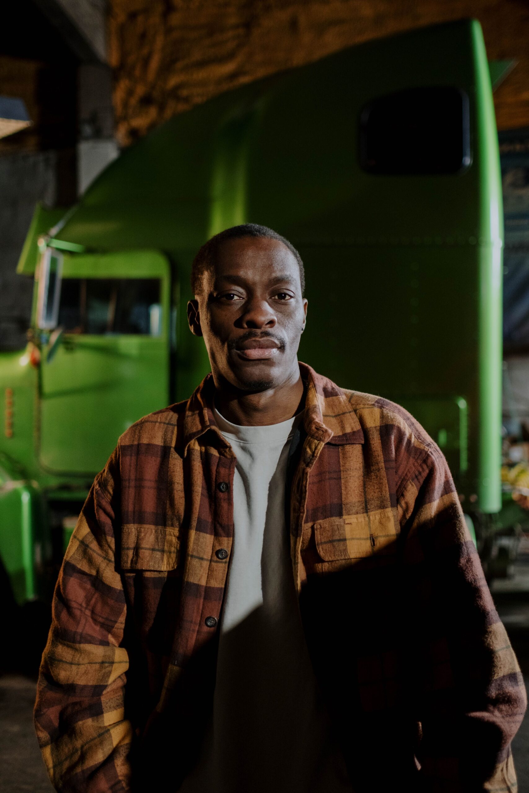 African American man posing confidently in front of a green truck indoors, wearing casual attire.